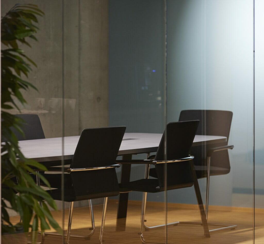 Besprechungsraum hinter einer Glasfront mit schwarzen Stühlen und Pflanze.