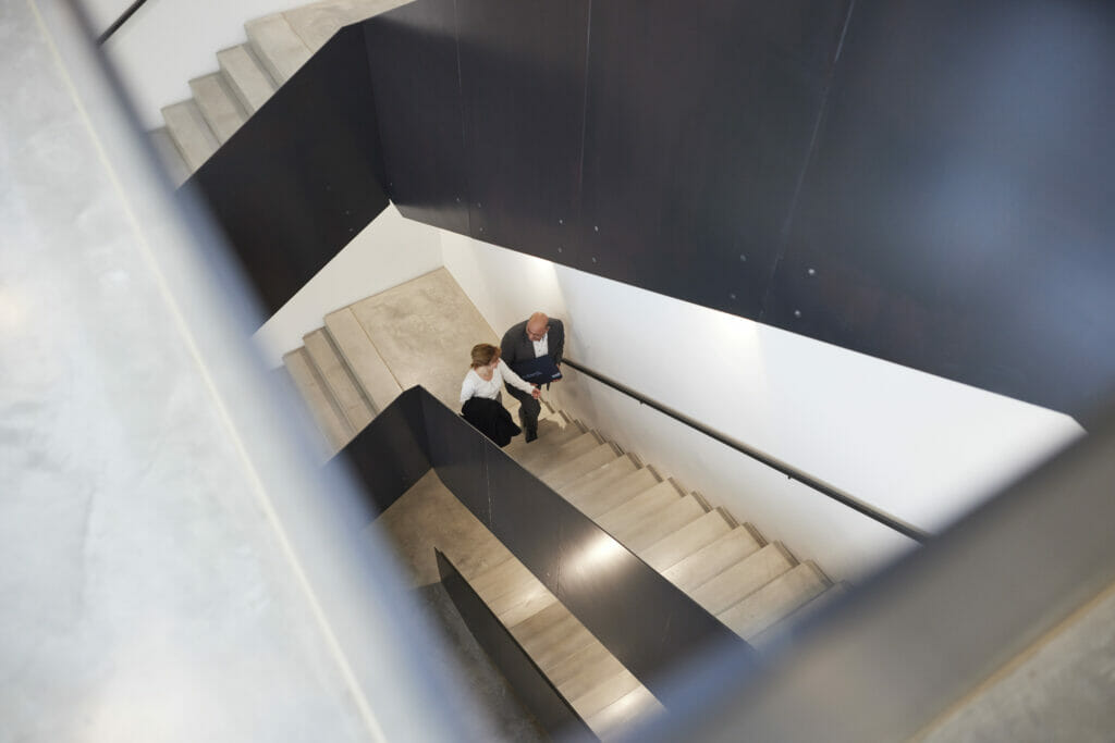 Anwalt und Anwaeltin, die durch das moderne, im Industrie-Design gestaltete, Treppenhaus der Anwaltskanzlei gehen.